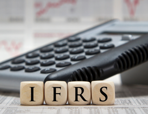 Calculator resting on financial documents with wooden blocks spelling ‘IFRS’ in front
