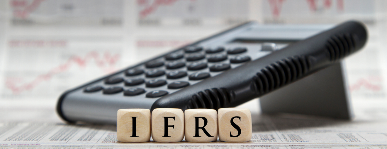 Calculator resting on financial documents with wooden blocks spelling ‘IFRS’ in front