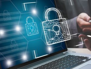 Laptop displaying digital padlock icons representing cybersecurity, with people using a tablet and stylus in the background