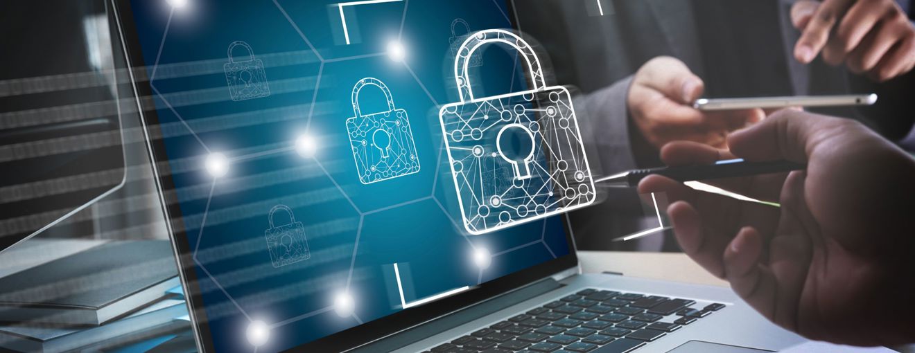 Laptop displaying digital padlock icons representing cybersecurity, with people using a tablet and stylus in the background
