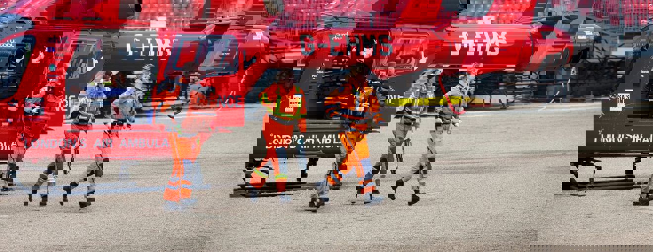 Air ambulance crew in orange flight suits walking away from a red helicopter during an emergency response