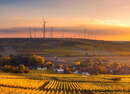 Sunset over a rural landscape with fields, vineyards, and wind turbines on the horizon