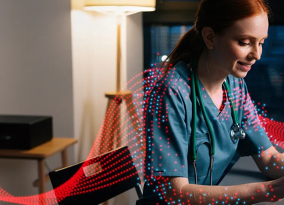 Healthcare professional in scrubs working on a laptop at a desk with digital wave graphics overlayed