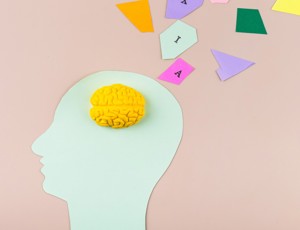 illustration of a human head silhouette with a yellow brain model inside and colourful geometric shapes emerging from it