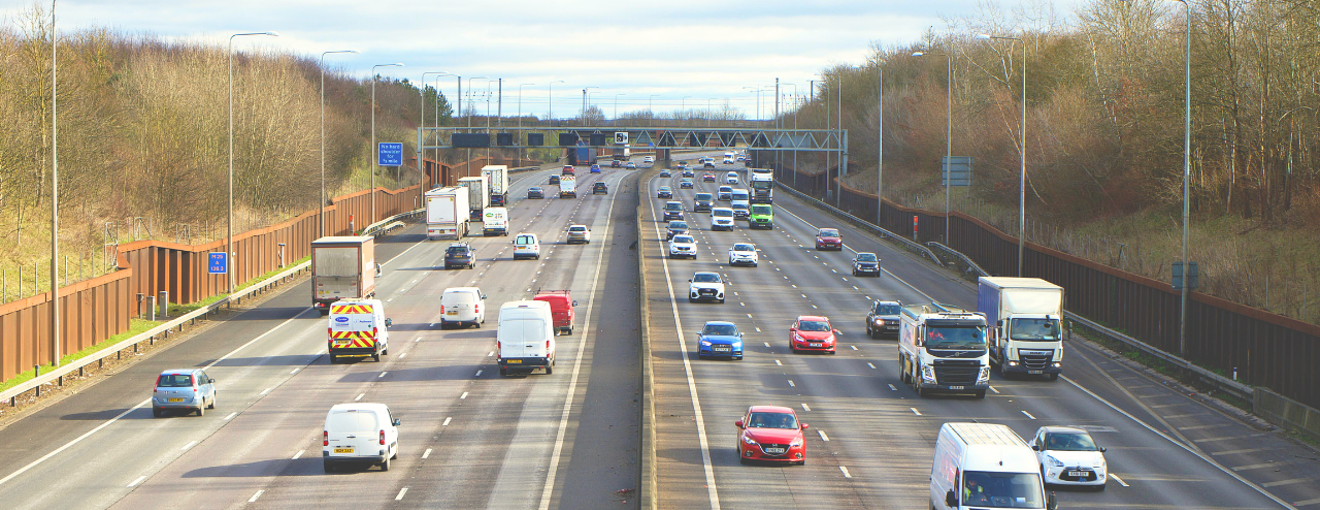 Busy multi‑lane motorway with cars, vans, and lorries travelling in both directions on a clear day