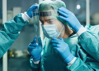 Medical staff wearing protective gowns, gloves, and face shields helping a colleague adjust their protective equipment