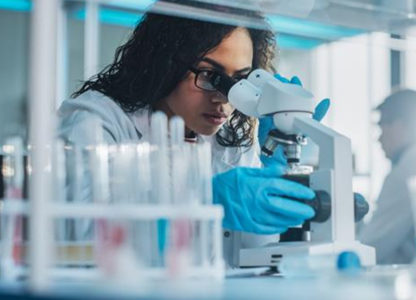 Scientist wearing gloves using a microscope in a laboratory with test tubes and equipment in the foreground